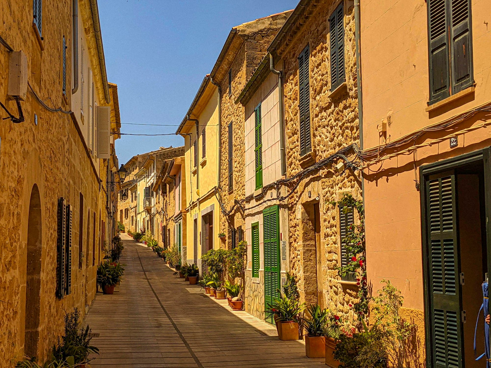 A narrow street inside the walled old town of Alcúdia with green shutters and stone facades, Mallorca