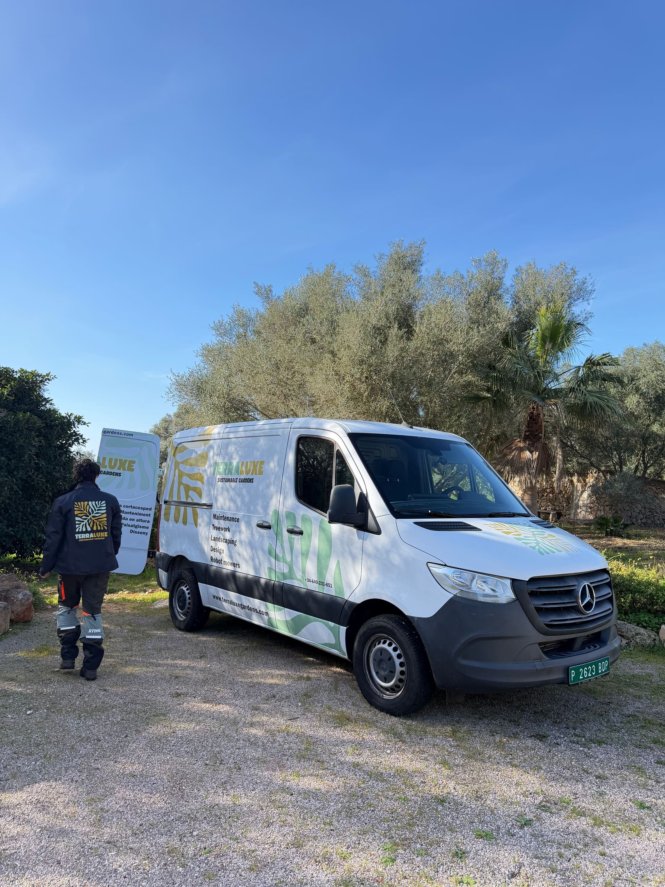 TerraLuxe-Gardens-Gärtner neben einem Elektro-Flottenwagen und einem Olivenbaum auf einer Finca auf Mallorca