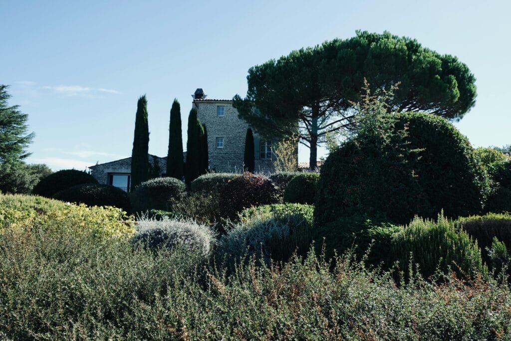 Stone house in Provence-Alpes-Côte d'Azur surrounded by lush greenery and trees under a blue sky.